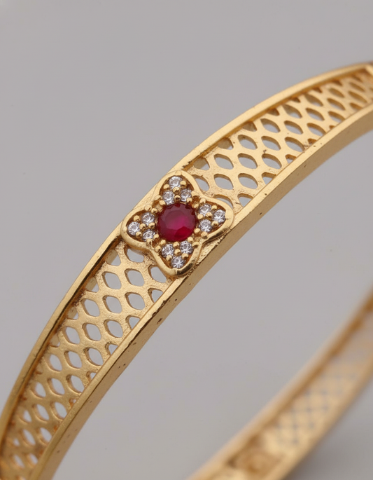 Gold bracelet with a red gemstone and diamond accents on a gray background