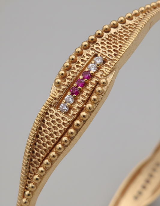 Gold bracelet with embedded gemstones on a gray background