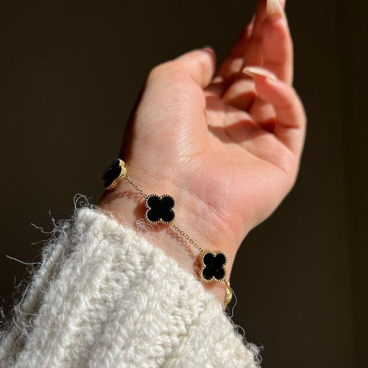 Hand wearing a bracelet with black clover-shaped charms against a dark background