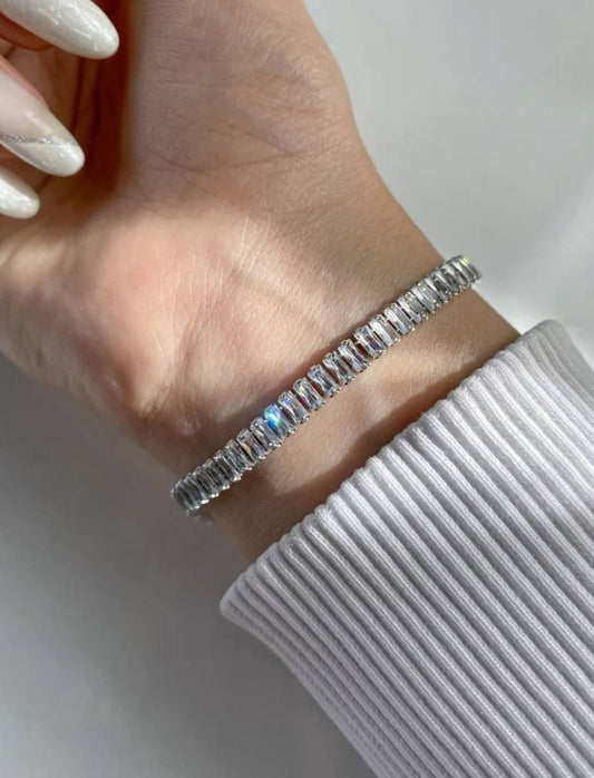 Silver bracelet on a wrist with a plain background