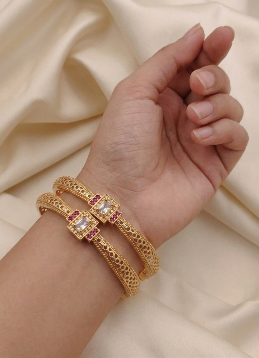 Gold bangle with gemstones on a hand against a beige fabric background