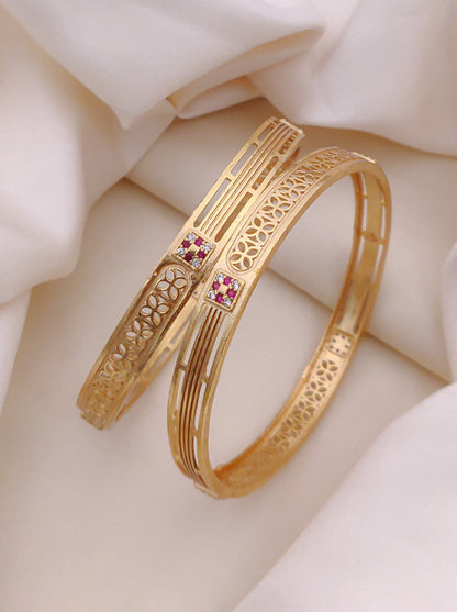 Gold bangles with intricate designs and small pink stones on a soft beige fabric background