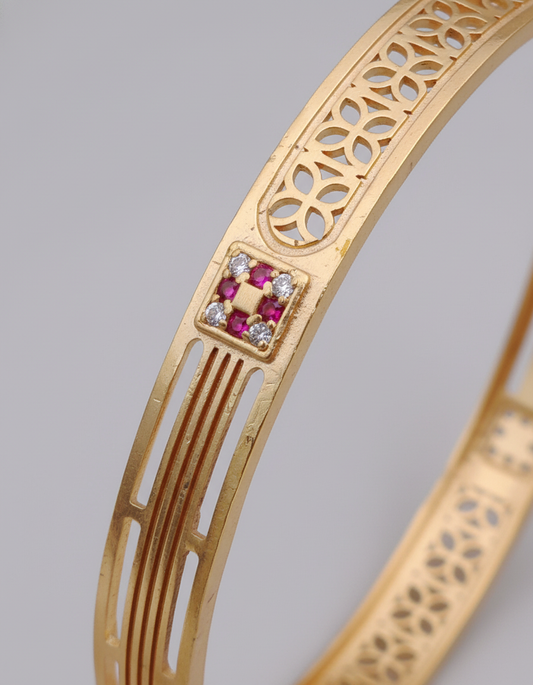 Gold bracelet with intricate design and embedded gemstones on a gray background