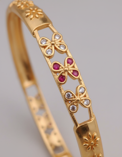 Gold bracelet with butterfly designs and red stones on a gray background