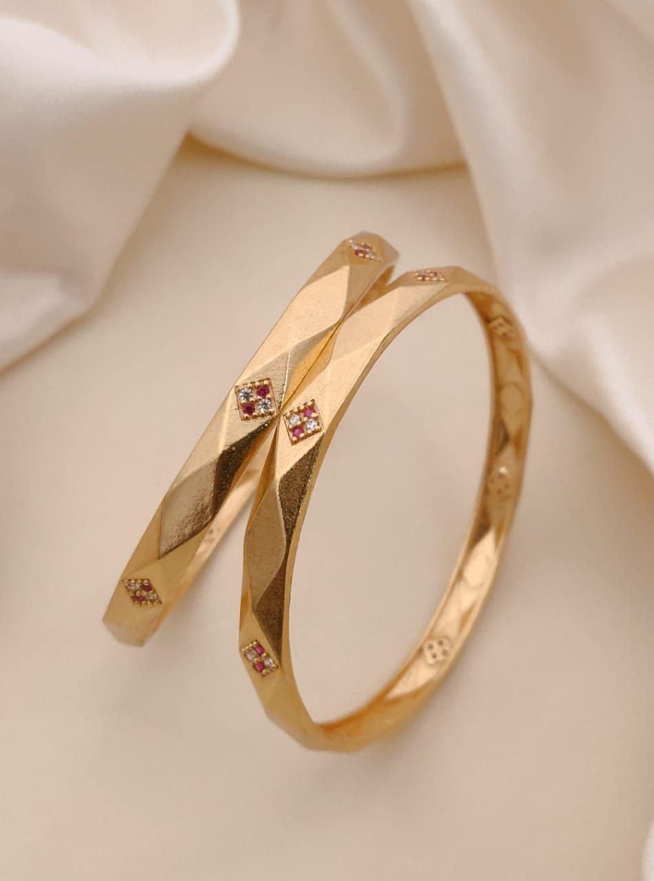 Gold bangle with embedded red gemstones on a soft beige fabric background.