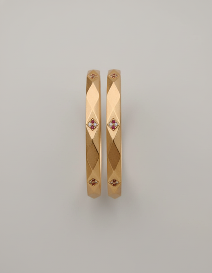 Gold bangles with embedded stones on a light gray background