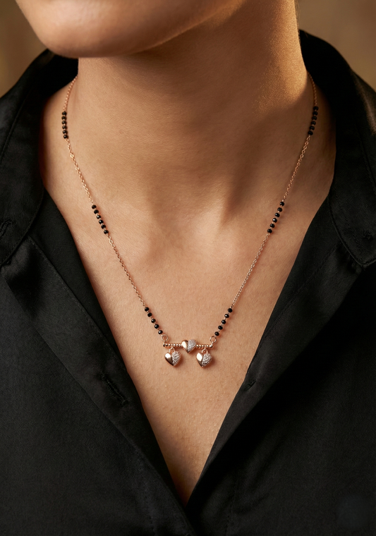 Necklace with black beads and rose gold accents on a person wearing a black shirt.