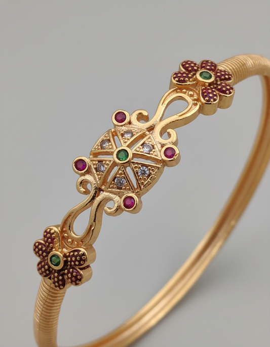 Gold bracelet with floral designs and gemstones on a gray background