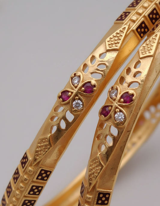 Gold bangles with gemstone inlays on a gray background