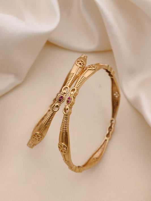 Gold bracelet with snake design and red gemstones on a beige fabric background