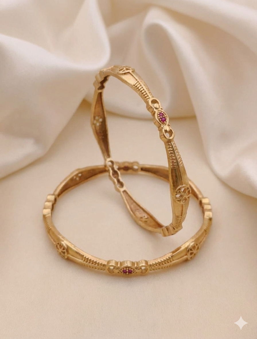 Gold bangles with red gemstones on a beige fabric background