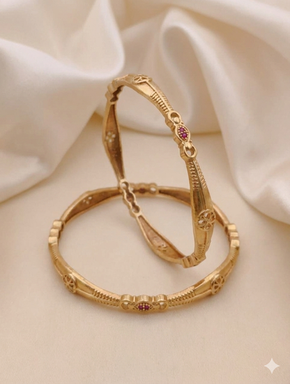 Gold bangles with red gemstones on a beige fabric background