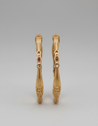 Pair of gold earrings with red gemstones on a gray background