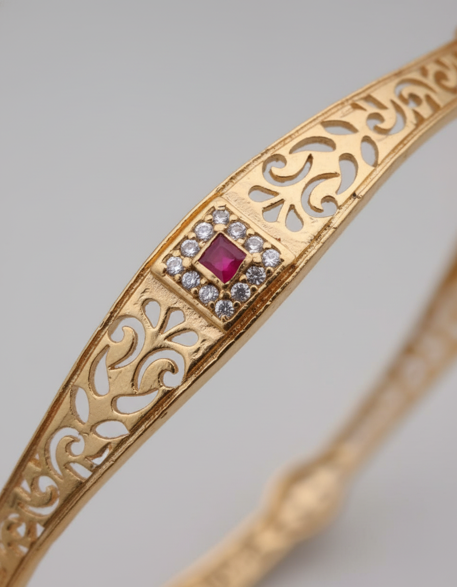 Gold bracelet with intricate design and a red gemstone on a gray background