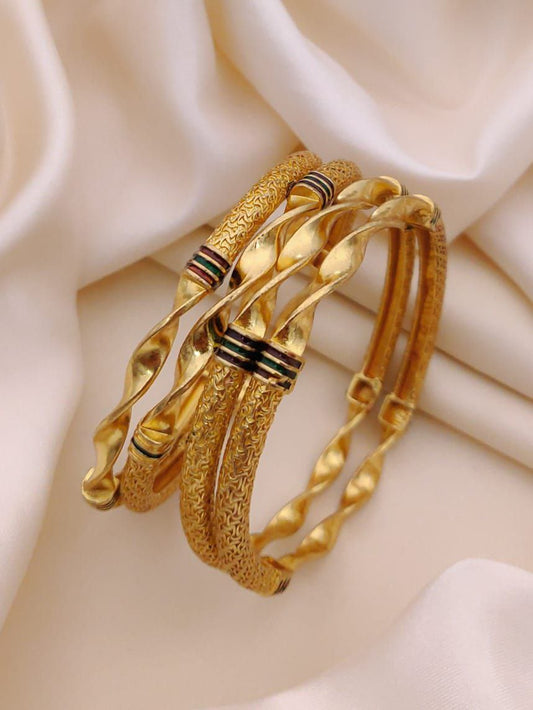 Four gold bangles with textured designs on a soft beige fabric background