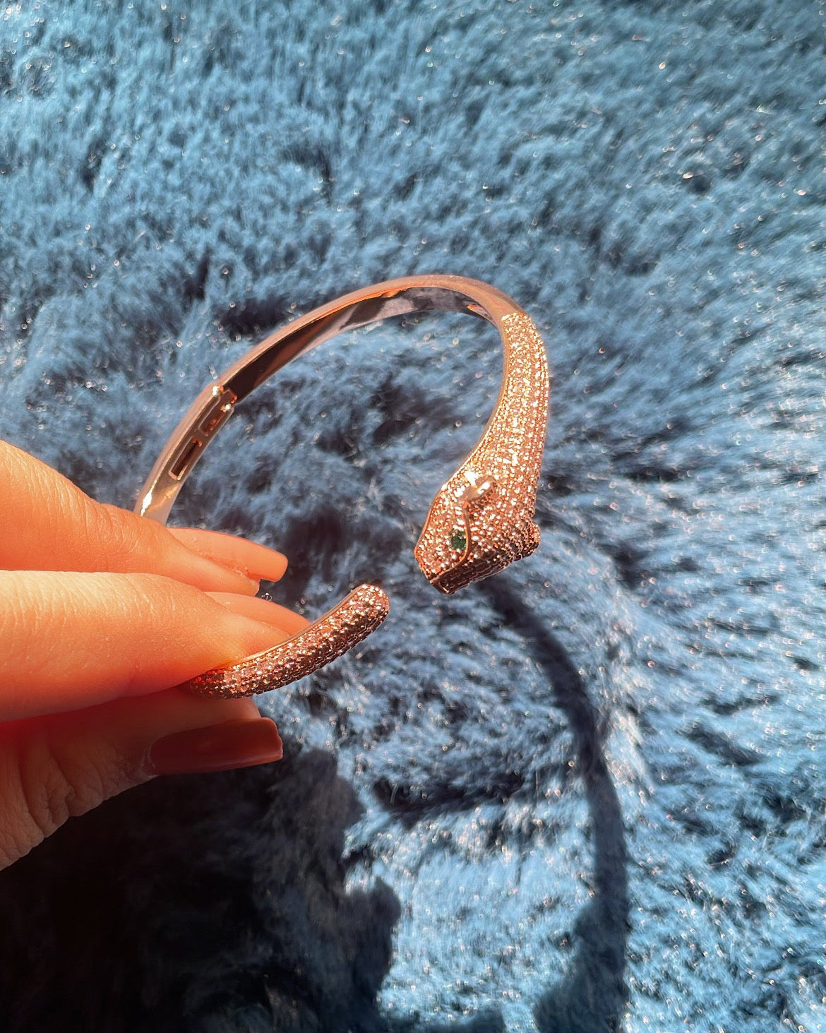 Rose gold bracelet held by a hand on a blue textured surface