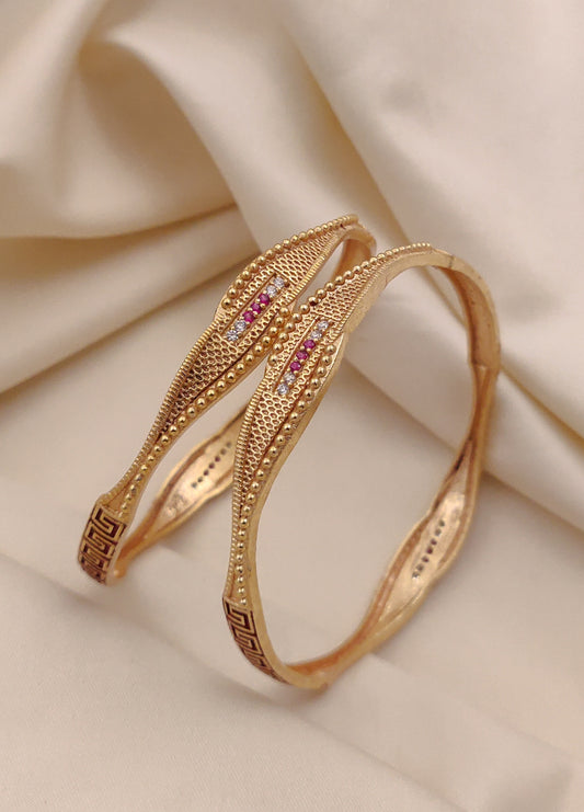 Gold Bangle with pink gemstones on a beige fabric background