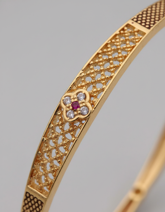 Gold bracelet with intricate design and gemstones on a gray background
