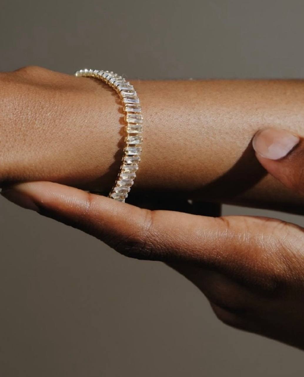Close-up of a hand wearing a diamond bracelet on a neutral background