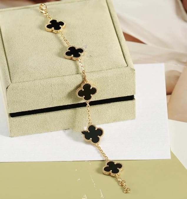 Gold bracelet with black clover-shaped charms on a beige jewelry box
