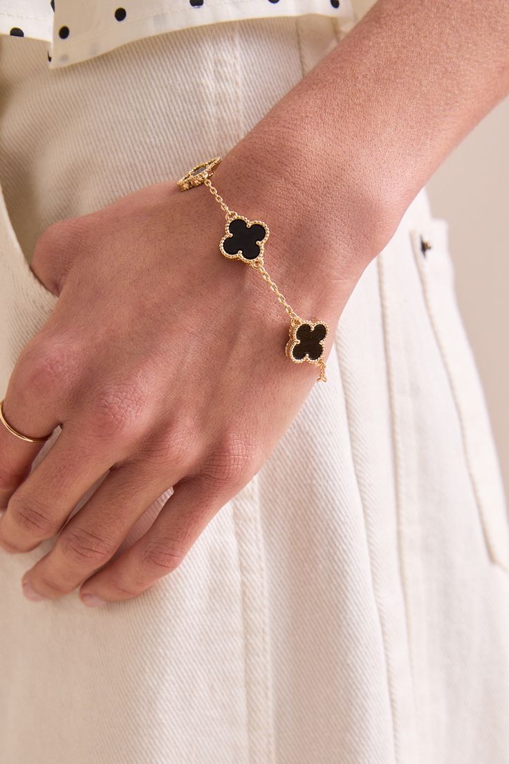 Gold bracelet with black clover charms on a wrist against a white background