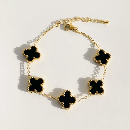 Gold bracelet with black clover-shaped charms on a light background