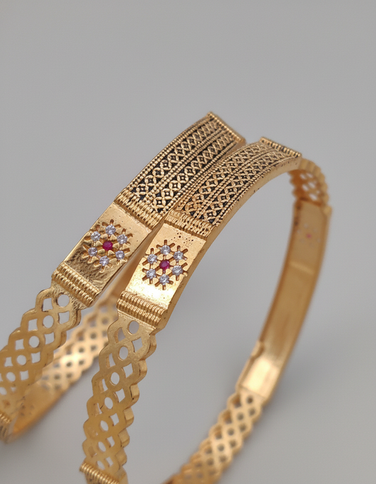 Gold bracelet with intricate designs and gemstones on a gray background