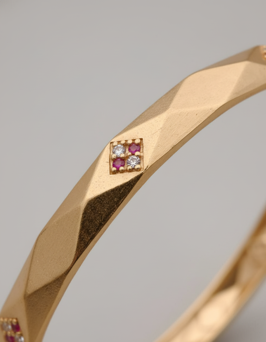 Gold bangle with diamond and ruby stones on a gray background