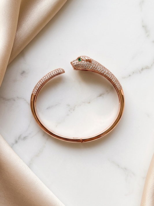Rose gold panther-shaped bracelet with green gemstone on a marble surface