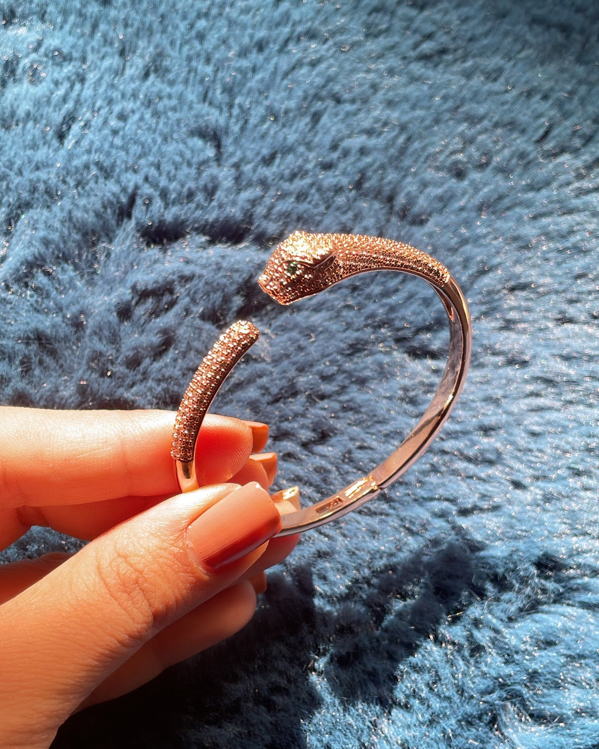 Hand holding a gold bracelet against a textured blue background