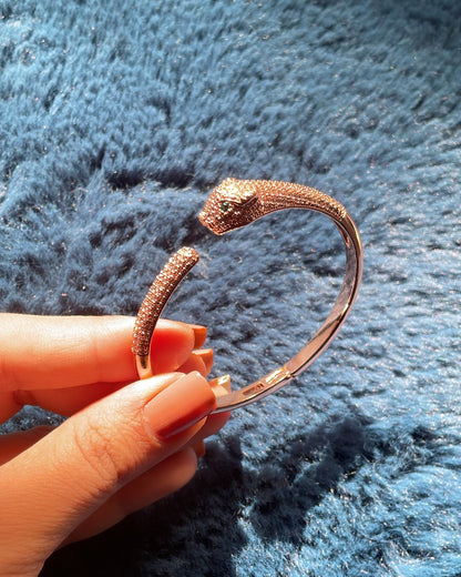Hand holding a gold bracelet against a textured blue background