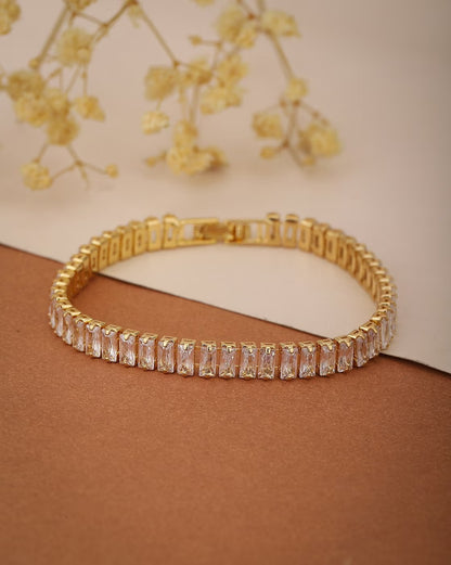 Gold bracelet with clear stones on a brown surface with yellow flowers in the background